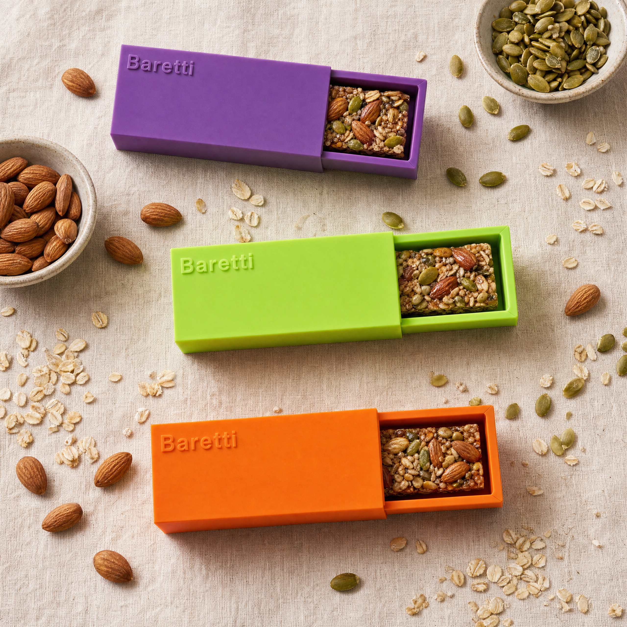 BarCraft reusable snack bar makers in purple, lime green, and orange displaying finished homemade nut and seed bars surrounded by raw almonds, oats, and pumpkin seeds